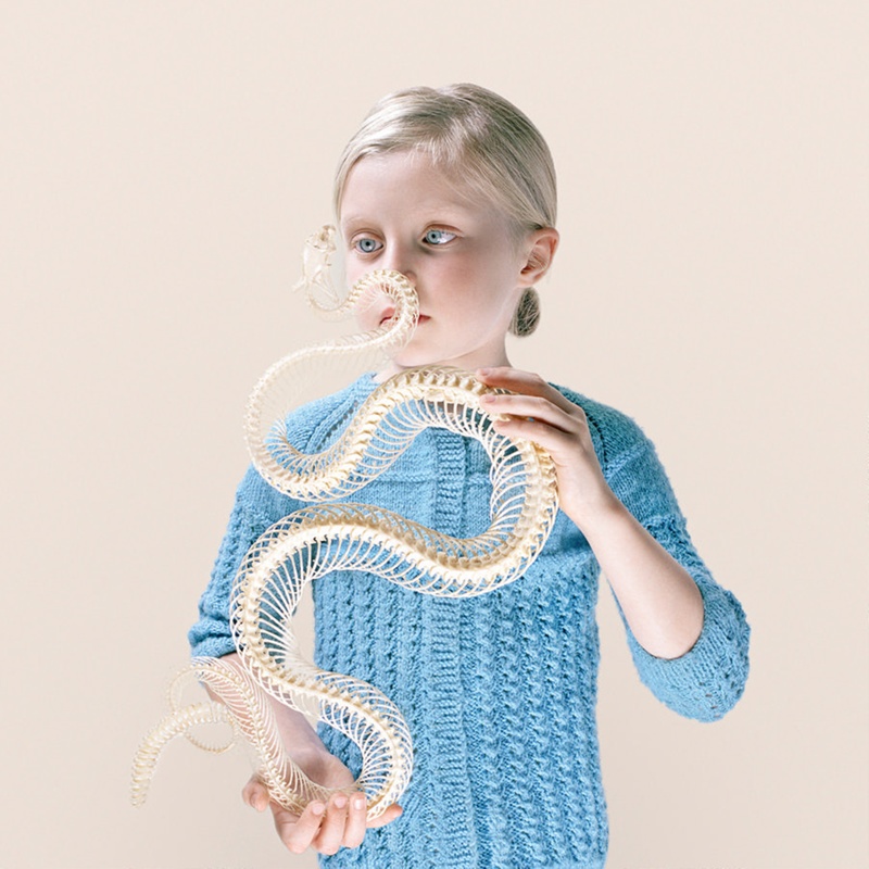 Photograph entitled "Rattlesnake blues" featuring a young girl in blue clothing holding the skeleton of a rattlesnake in a position where it would attack her face.